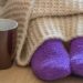 Cold concept with teacup near the legs which are covered with fluffy warm blanket and wearing fluffy warm purple socks
