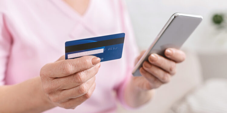 Senior woman shopping online on smartphone, paying with credit card, closeup